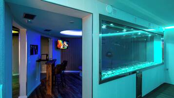 Ein modernes Zimmer mit einem großen Aquarium, Holzboden und einer Sitzecke mit Stühlen.