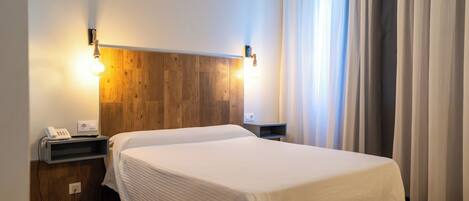 A hotel room with a wooden headboard, a white bedspread, a bedside table with a phone, and a nightstand.