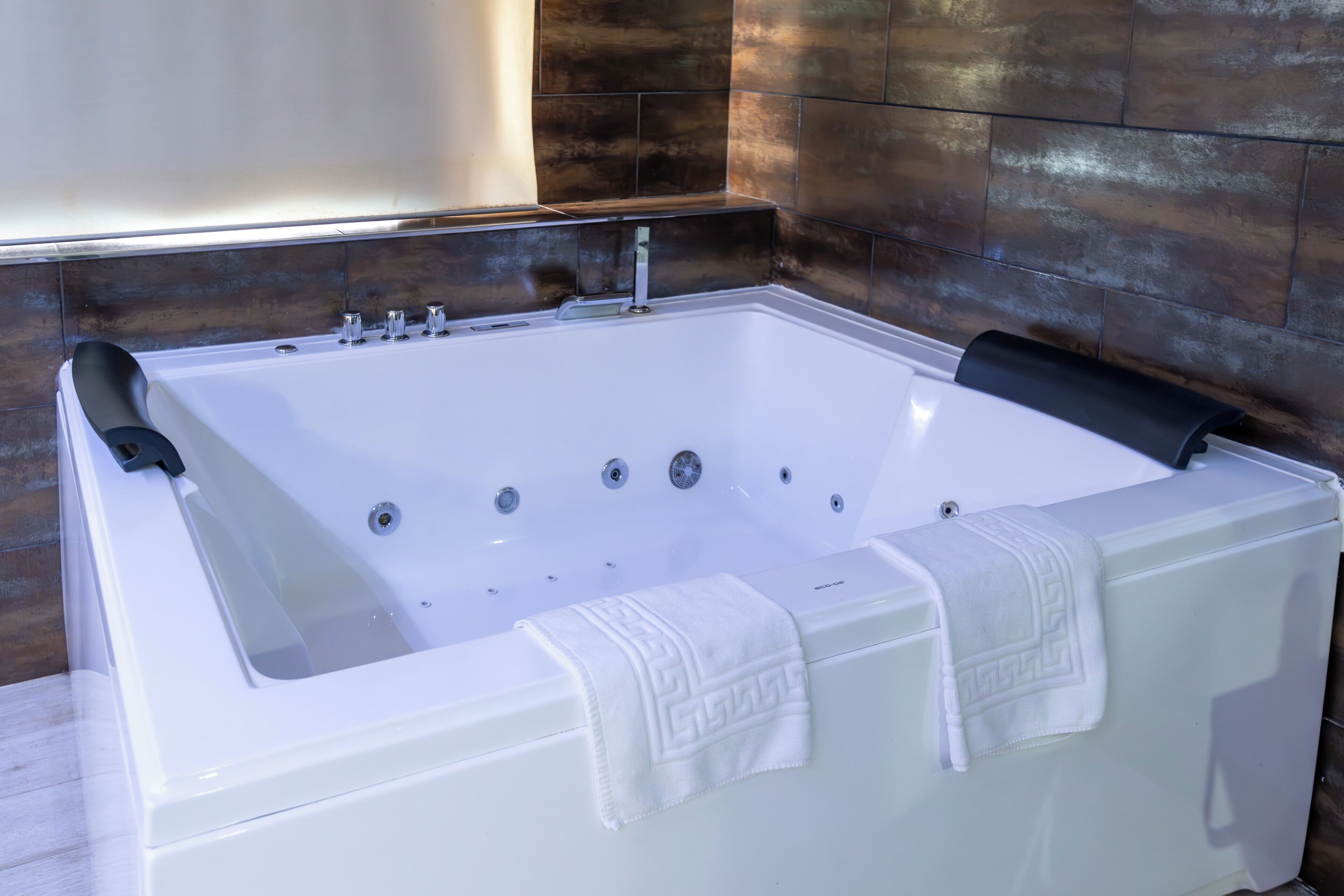 Ett stort, rektangulärt bubbelbad med flera massagemunstycken, placerat framför en bakgrund av mörka, strukturerade kakelplattor.