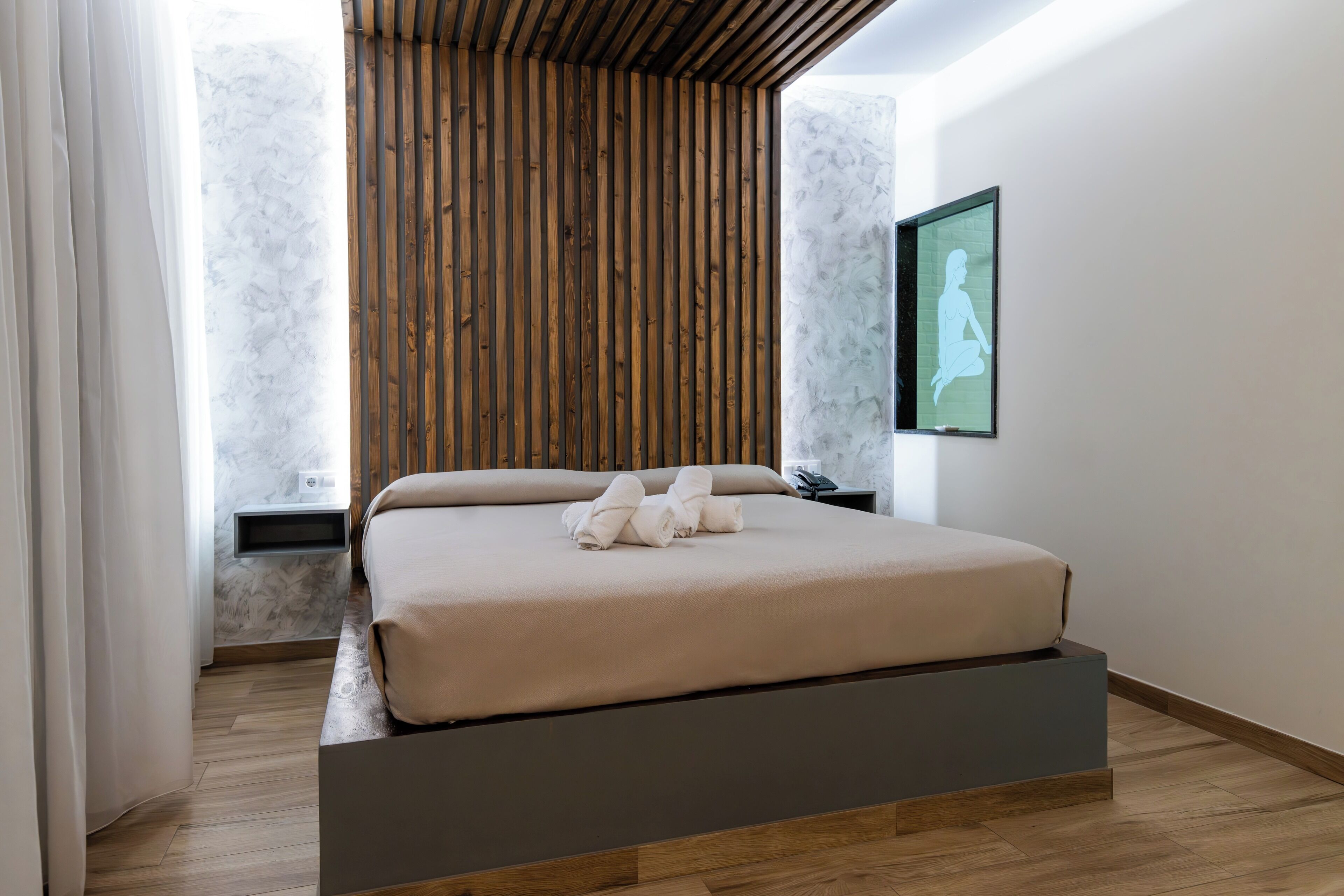 A modern bedroom with a bed, wooden slats, a marble wall, and a framed picture.