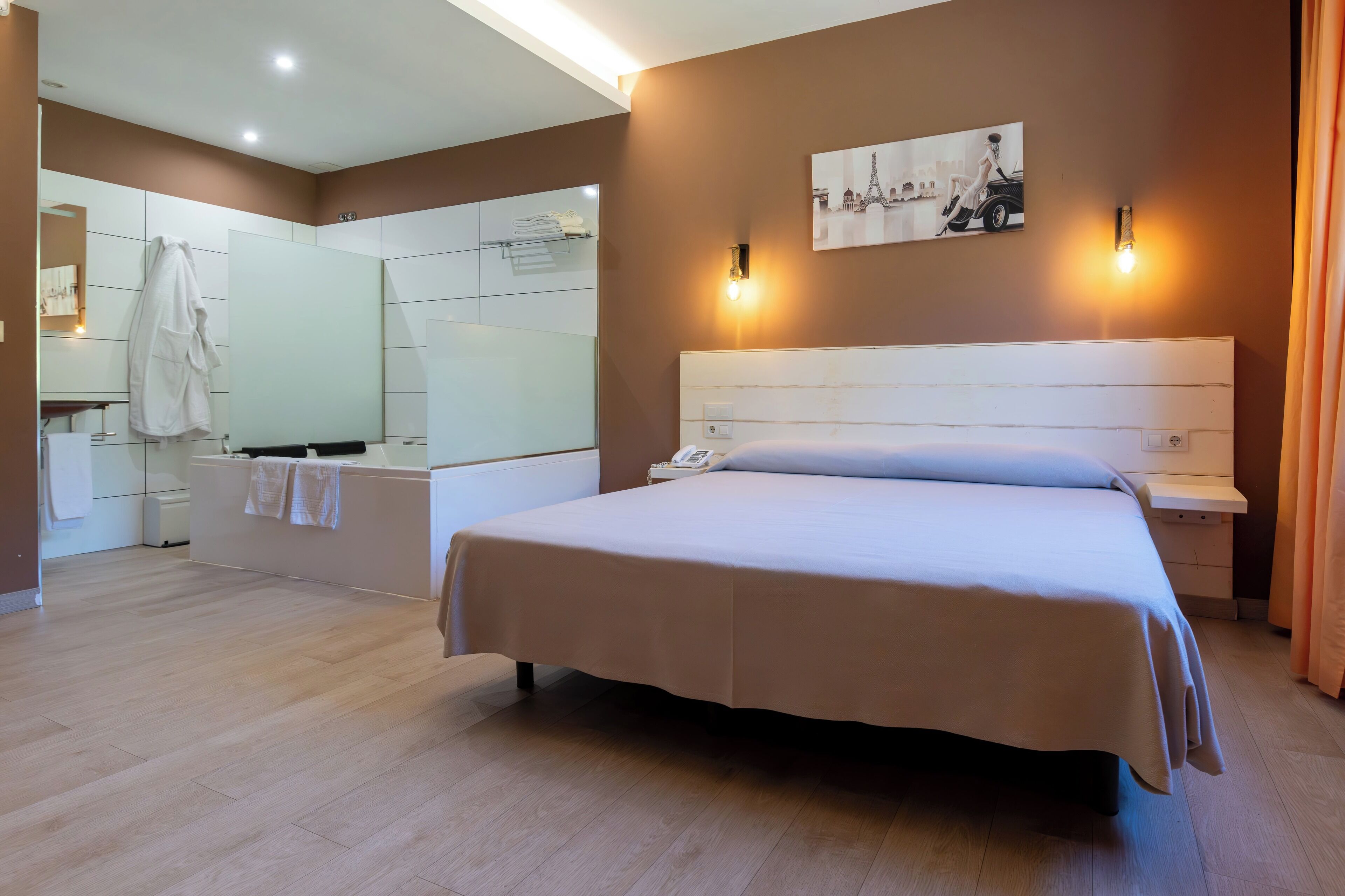 A modern hotel room with a large bed, a bedside table, a mirror, and a bathroom visible in the background.