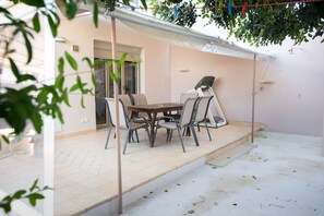 A covered patio with a table and chairs, a treadmill, and a door leading to an interior space.
