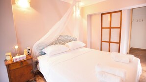 A neatly made bed with white linens and a canopy, a bedside table with a lamp, and a wooden door with glass panels. - Cozy beachside retreat in Kalamaki - steps from the sea (Neo Kalamaki)