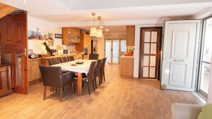 A spacious dining area with a large table and chairs, wooden cabinets, and a kitchen in the background. - Cozy beachside retreat in Kalamaki - steps from the sea (Neo Kalamaki)