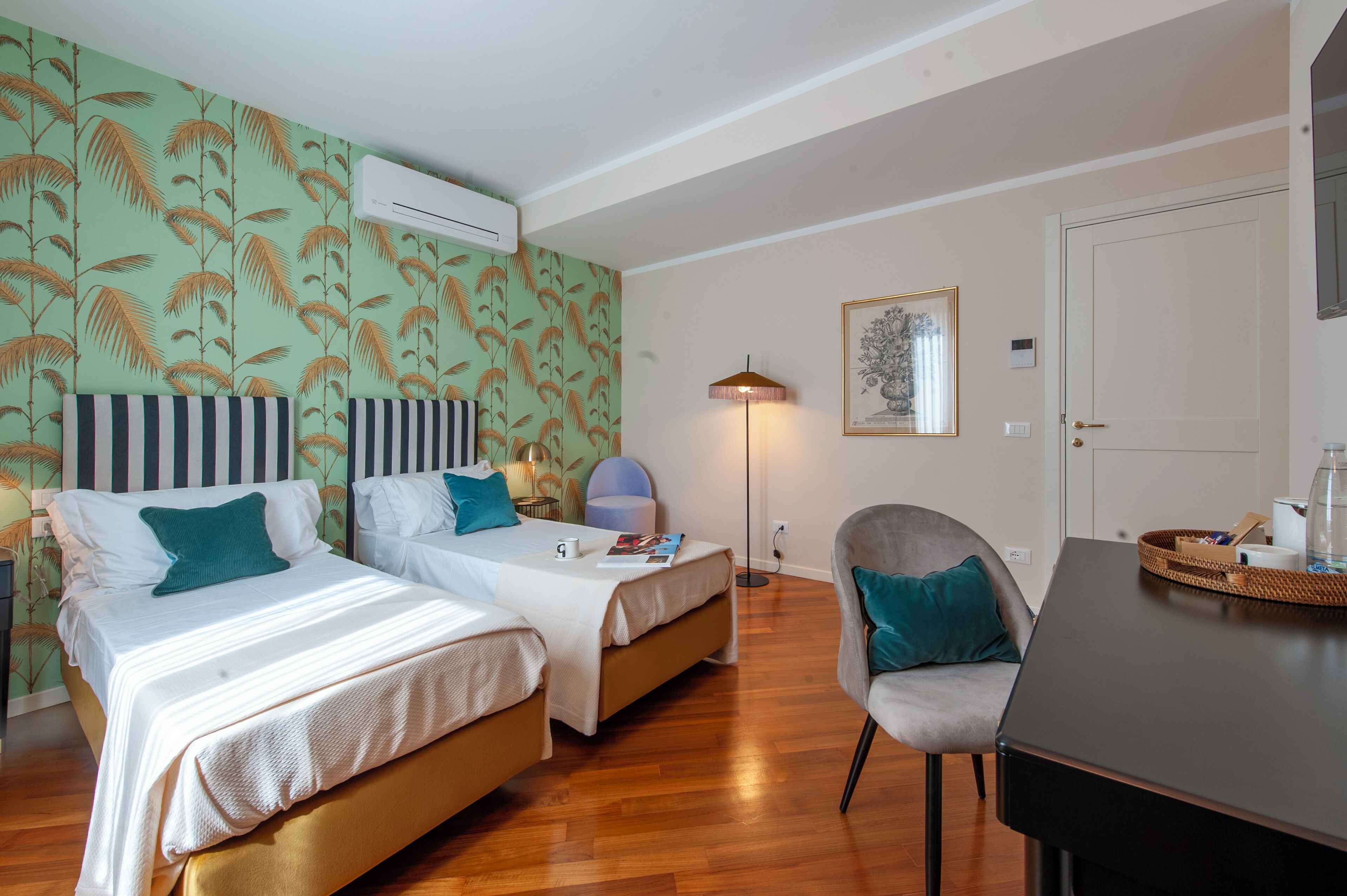 Habitación de hotel con dos camas, un escritorio, una silla, una lámpara y un cuadro en la pared.