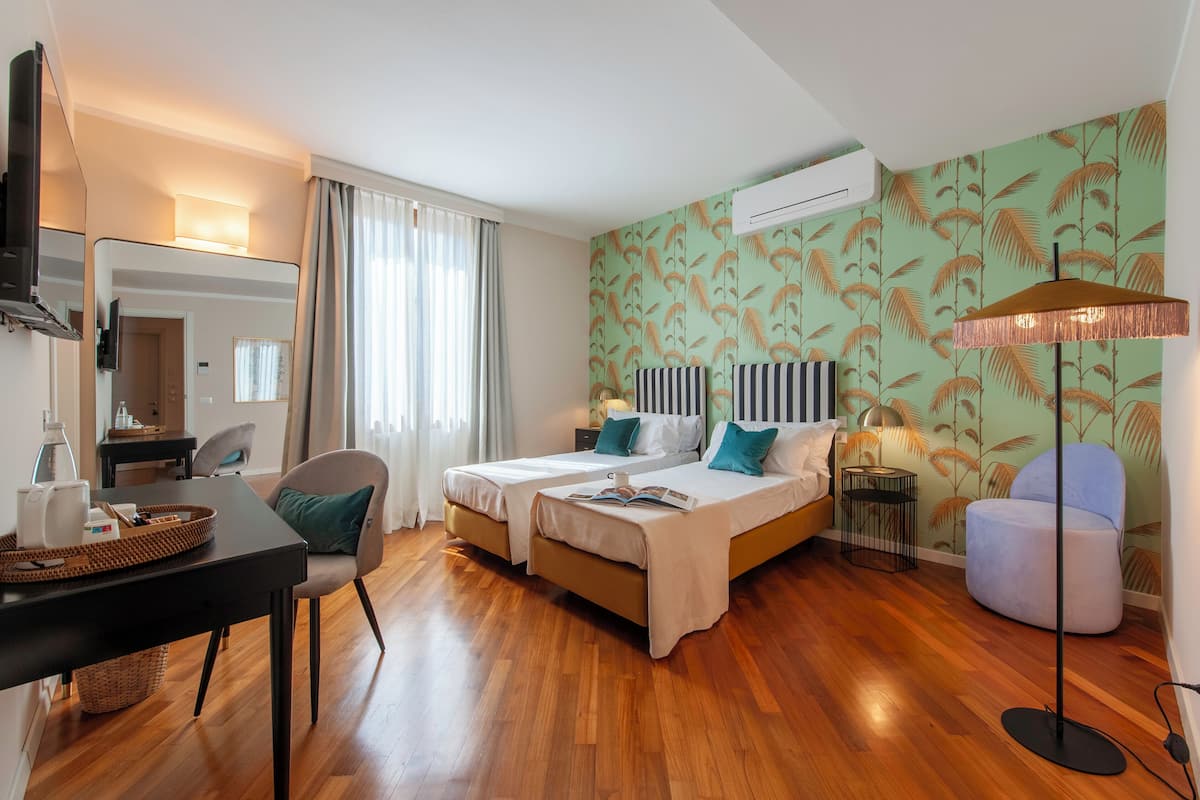 A hotel room with two beds, a desk, a chair, a lamp, and a wall with a leaf pattern.