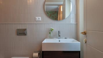 A bathroom with a white sink, a mirror, a towel dispenser, and a toilet.