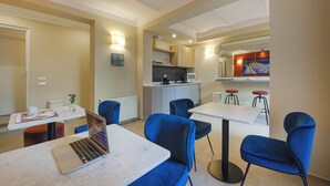 Une chambre d’hôtel moderne dotée d’un coin repas, d’une kitchenette et d’un espace salon avec des chaises bleues et une table blanche.