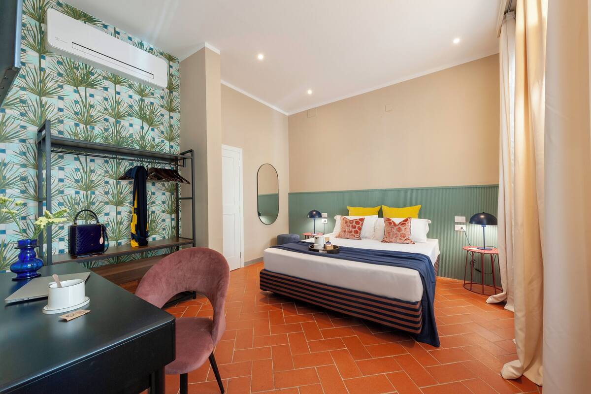 Une chambre d’hôtel équipée d’un lit, d’un bureau, d’une chaise, d’un miroir, d’une lampe et d’une fenêtre avec des rideaux.