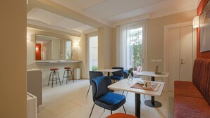 A modern dining area with a white table, blue chairs, and a red sofa. There is a kitchen area with a refrigerator, sink, and stools. - La Corticina - Rooms & Suite - Firenze (Florence)