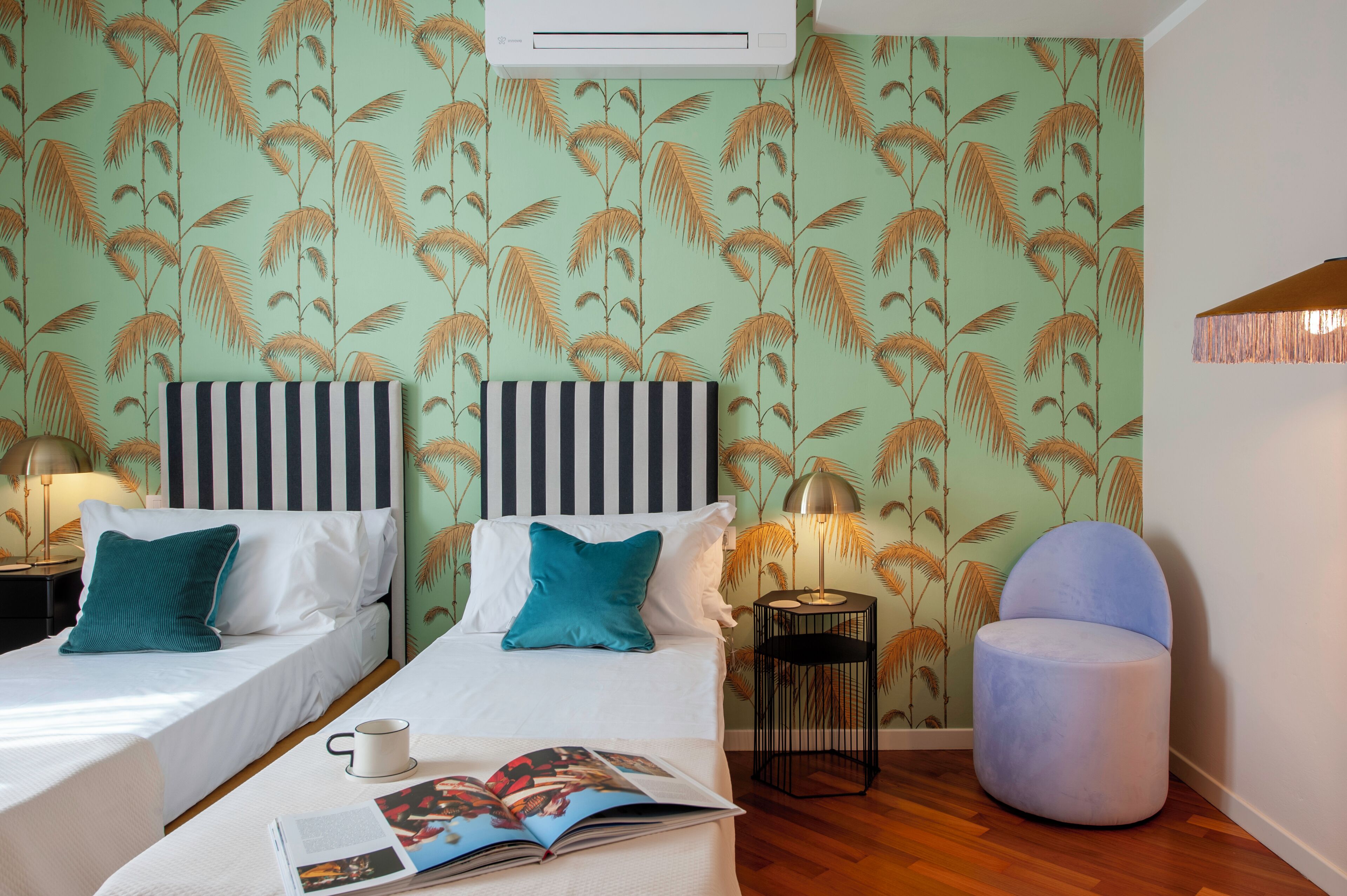 A hotel room with two beds, a small table with a magazine, a lamp, and a chair.