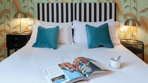 Un lit bien fait, avec du linge de lit blanc et des coussins turquoise, un magazine posé sur le lit, et deux tables de chevet avec des lampes.