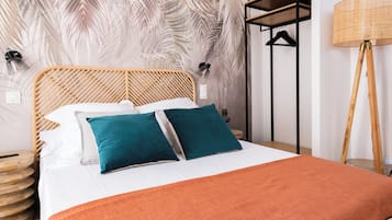 Una cama bien hecha con cabecera de madera, dos almohadas color turquesa y una manta naranja.