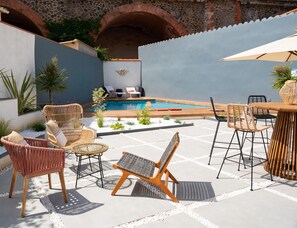 Zona de piscina amb mobiliari de vimet, una piscina i una paret de pedra.