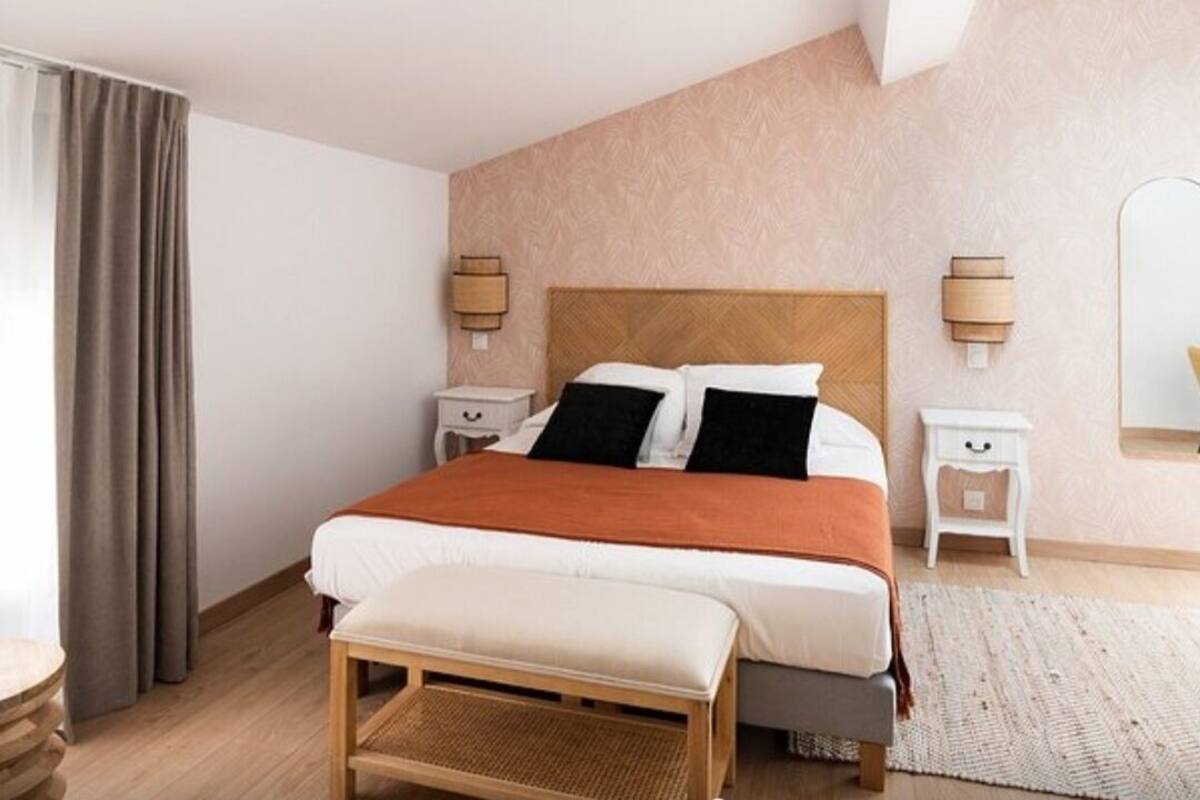 Ein Schlafzimmer mit Bett, Nachttischen, einer Bank, einem Spiegel und einem Fenster mit Vorhängen.