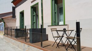 Et hotels ydre med en brobelagt terrasse, udendørs siddepladser med borde og stole, samt grønt indrammede vinduer.