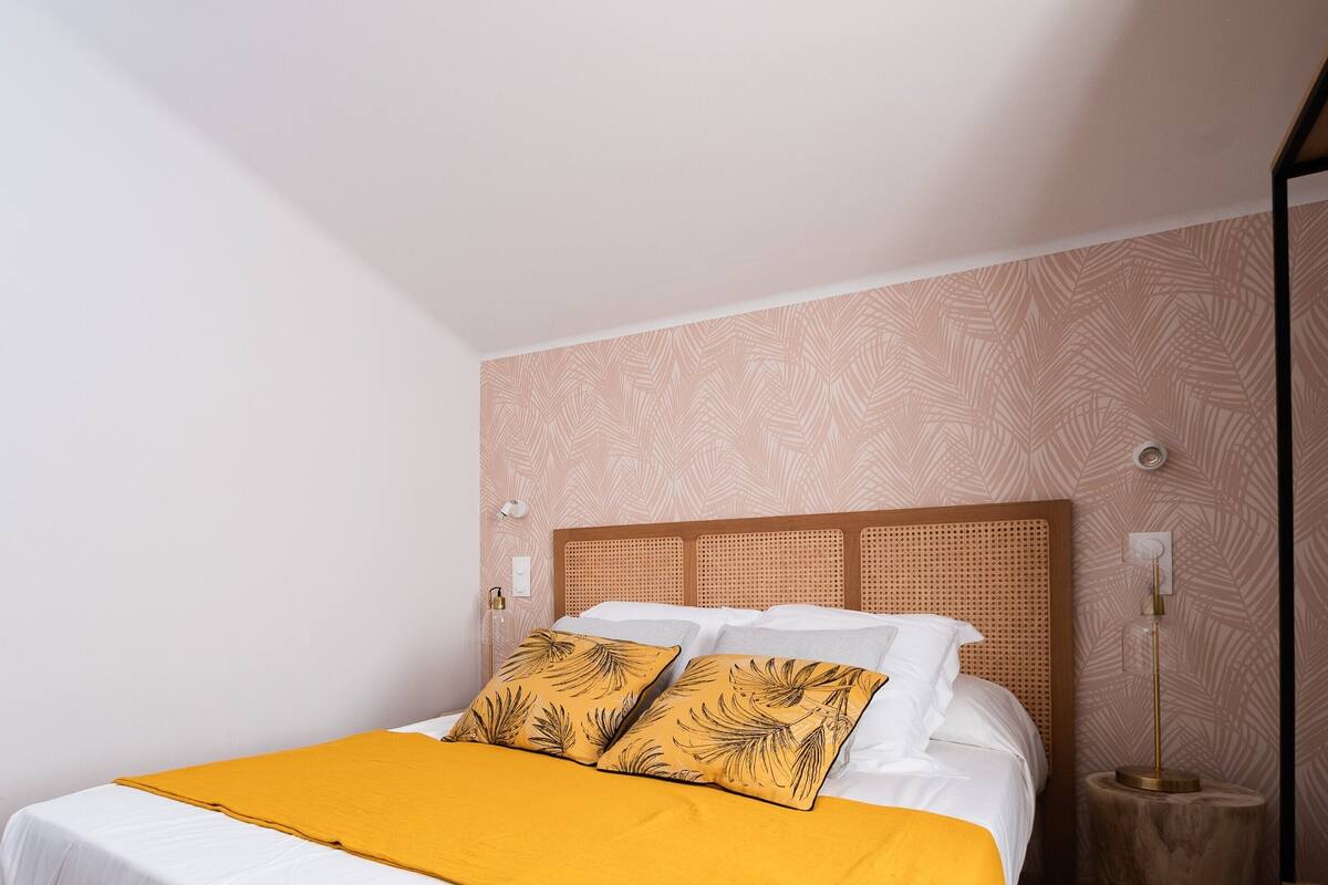 Ein ordentlich bezogenes Bett mit einem Holz-Kopfteil, einer gelben Decke und zwei passenden Kissen.