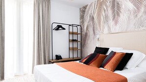 A modern hotel room with a bed, a bedside table with a phone, a wall-mounted shelf with hangers, and a large window with curtains. - Hôtel Le Ribéral (Cerbère)