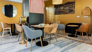 A modern dining area with a round table, wicker chairs, and a black sofa. - Hôtel Le Ribéral (Cerbère)