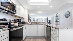 A modern kitchen with white cabinets, a stainless steel range hood, and a granite countertop. - Direct Gulf Front Ground Floor Condo | Steps to the Gulf and Pet-Friendly (Sanibel)