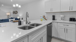A modern kitchen with white cabinets, a double sink, and a coffee maker.