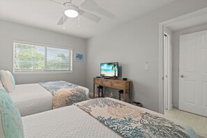 Ein Schlafzimmer mit zwei Betten, einem Fernseher auf einem Holzständer, einem Deckenventilator und einer Tür.