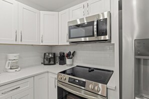 A modern kitchen with white cabinets, a stainless steel microwave, an induction cooktop, and a built-in oven.