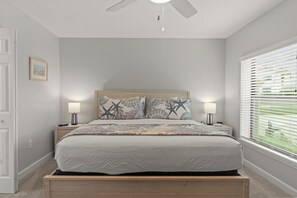 A bedroom with a bed, nightstands, a ceiling fan, and a window with blinds. - Coquina Beach 5C: Your Remodeled Island Getaway with Pool, Tennis & Sunshine! (Sanibel)
