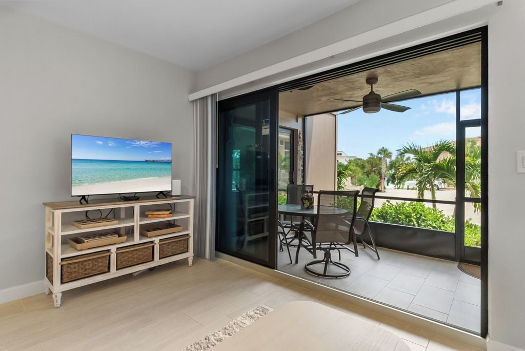 A modern living room with a television, a sliding glass door leading to a balcony with outdoor furniture.