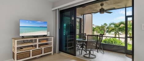A modern living room with a television, a sliding glass door leading to a balcony with outdoor furniture.