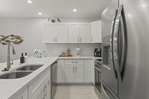 A modern kitchen with stainless steel appliances, white cabinetry, and a built-in dishwasher.
