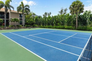 Una cancha de tenis con una red, rodeada de vegetación y un edificio.