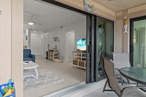 A modern living room with a glass door leading to a balcony, a blue sofa, a coffee table, and a TV.