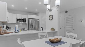 A modern kitchen with white cabinetry, stainless steel appliances, and a dining area with a white table and chairs.