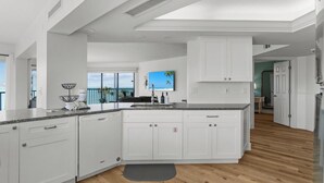 A modern kitchen with white cabinets, a granite countertop, and a view of the ocean. - Stunning Gulf-Front 3BR Condo with Panoramic Views – Newly Renovated! (Sanibel)