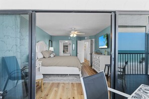 Een slaapkamer met een bed, nachtkastjes, een plafondventilator en uitzicht op het strand door een schuifdeur.