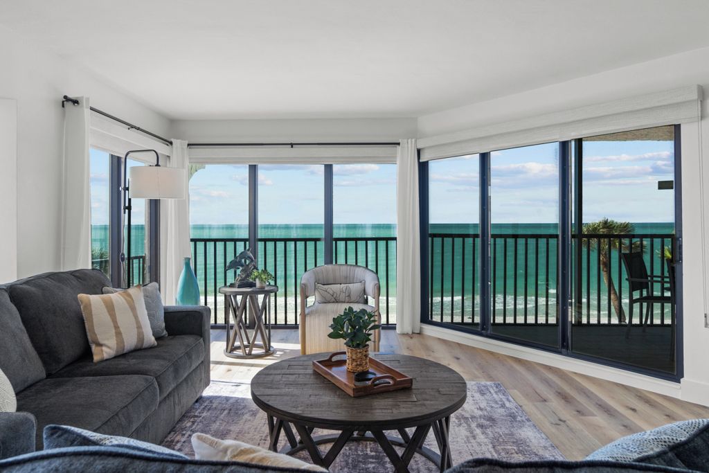 A spacious living room with a large sliding glass door leading to a balcony overlooking the ocean.