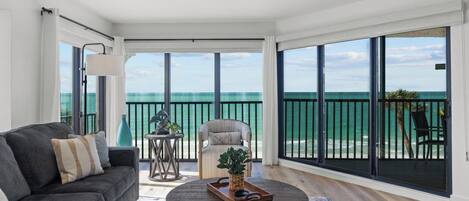 A spacious living room with a large sliding glass door leading to a balcony overlooking the ocean.