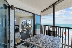 Een balkon met een tafel en stoelen met een patroon, met uitzicht op een strand en een helder zicht op de oceaan en de verre kustlijn.
