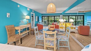 A room with a round table, chairs, a hanging light fixture, and a view of the outdoors.