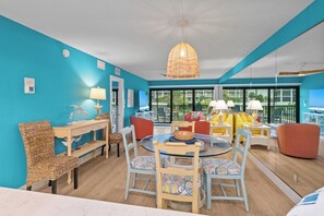 A room with a round table, chairs, a hanging light fixture, and a view of the outdoors.