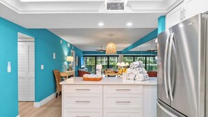 A modern kitchen with a large island, stainless steel appliances, and a view through the windows.