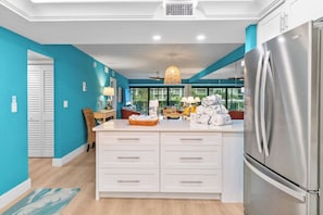 A modern kitchen with a large island, stainless steel appliances, and a view through the windows.