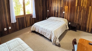 Een kamer met houten lambrisering, twee bedden, een klein tafeltje en een raam met gordijnen.