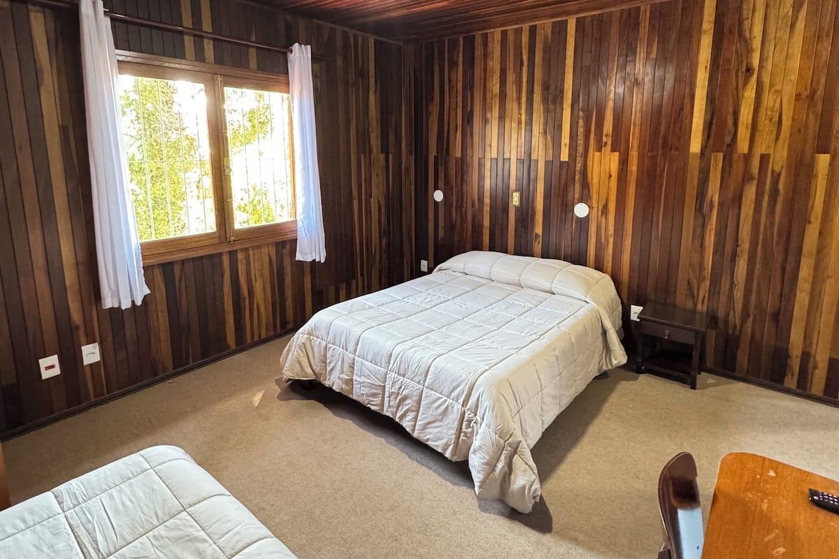 Una habitación con paneles de madera, dos camas, una mesita y un ventanal con cortinas.