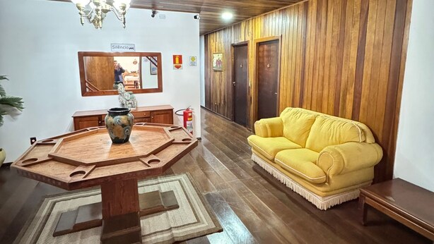 Een eetgedeelte met een houten tafel en stoelen, een gele bank en een kroonluchter.