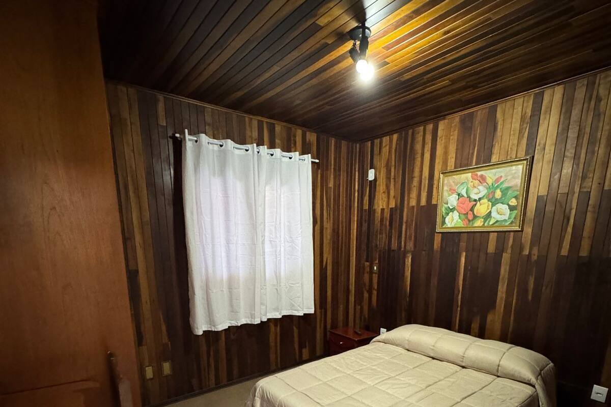 Un dormitorio con techo de madera, una cama con edredón blanco, una silla de madera y un cuadro en la pared.