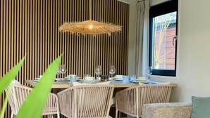 Un comedor con pared de listones de madera, una mesa preparada para cuatro personas con sillas blancas y una lámpara colgante.