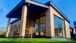 Una casa moderna con un gran ventanal, fachada de madera y un jardín cubierto de césped.