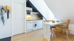 Una cocina compacta equipada con microondas, lavadora y mesa de comedor de madera con sillas.